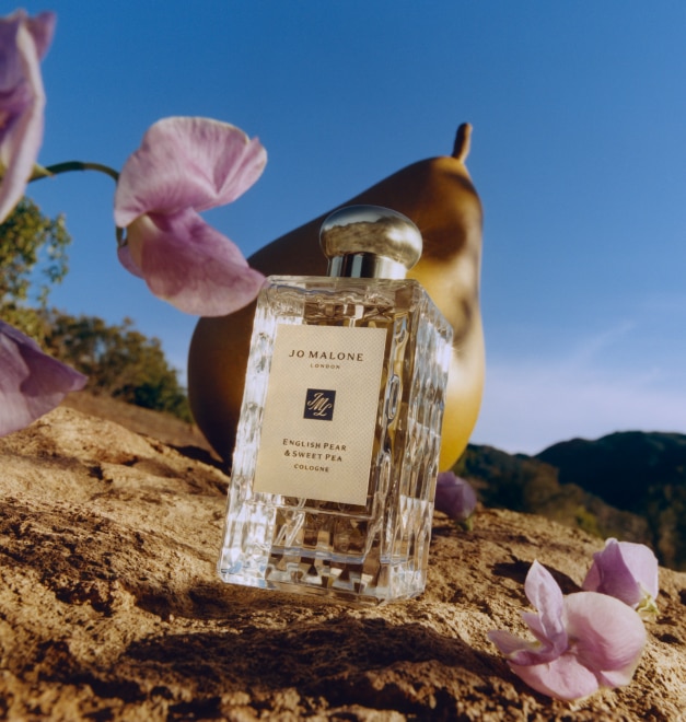 Pink sweet pea flowers and English Pear & Sweet Pea cologne 100ml bottle in front of big pear prop, on golden rocky hillside.